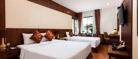 A hotel room with two beds, wooden paneling, a TV, a desk, and a window with curtains.