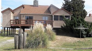 A two-story wooden house with a balcony, a chimney, and a large tree in the background.