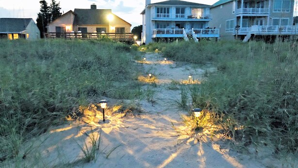 A pathway with sand and grass leading to a house with a balcony.