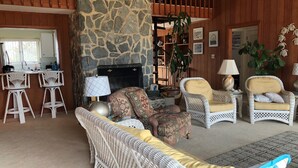 A cozy living room with wicker furniture, a stone fireplace, and a kitchen area with bar stools.