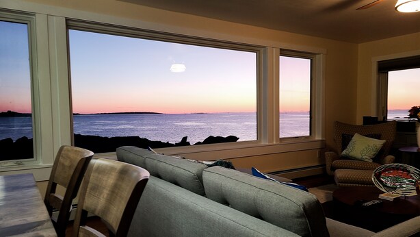 Un salón con vistas al océano al atardecer, ventanas amplias y un sofá.