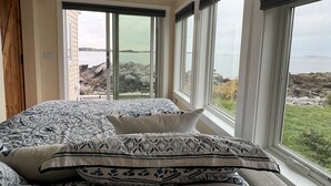 Un dormitorio con cama, ventanas amplias y vista al mar.