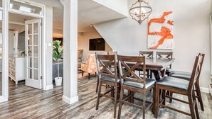 A dining area with a wooden table and chairs, a chandelier, and a large abstract painting on the wall. - #1 Rare 4Br Lux True Ski in Out @5 lifts Pool/Spas/Gym/WD/FP/Parking Near Main! (Park City)
