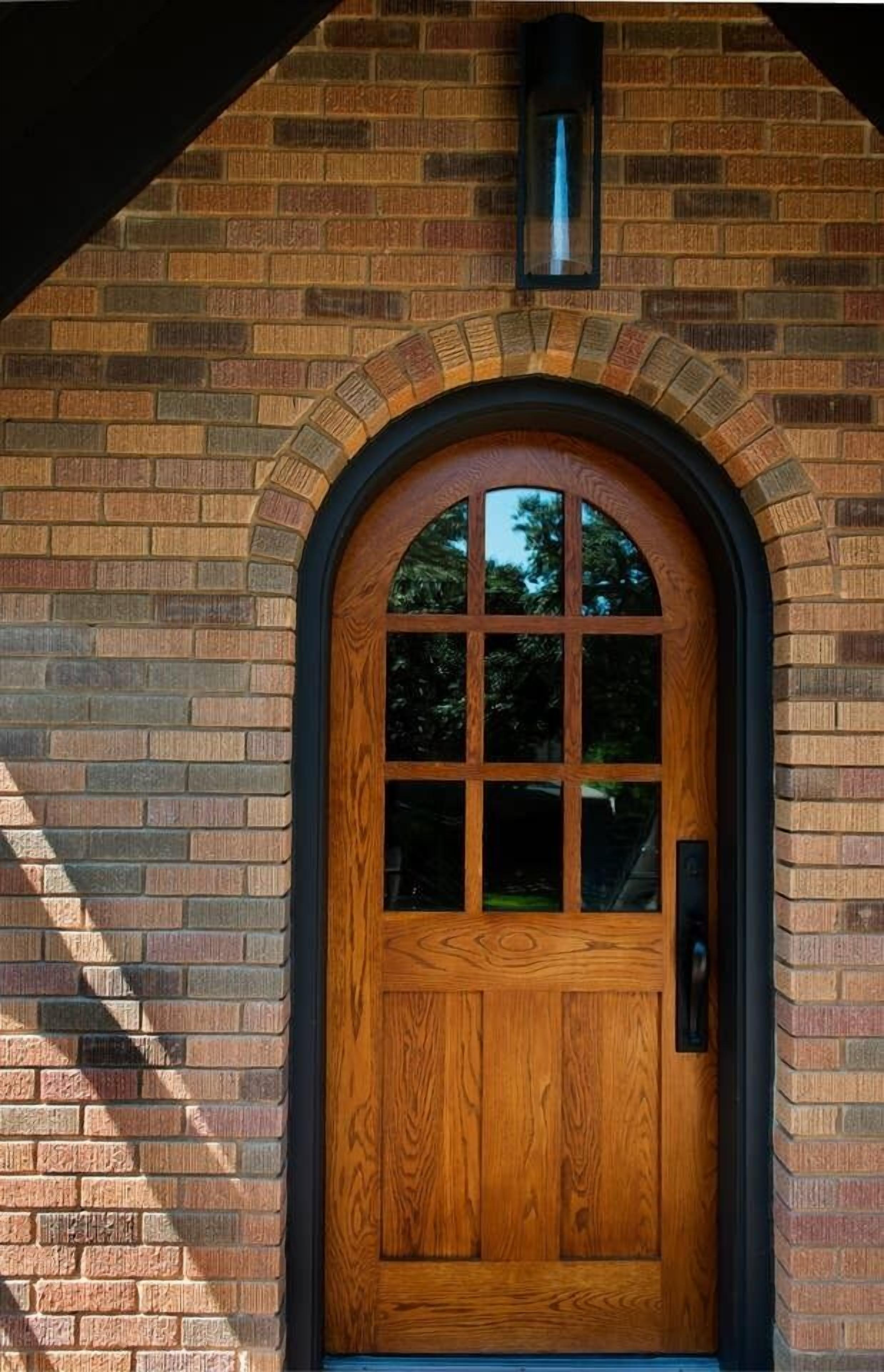 A wooden door with a glass panel, set in a brick wall with a black arch and a lantern above.