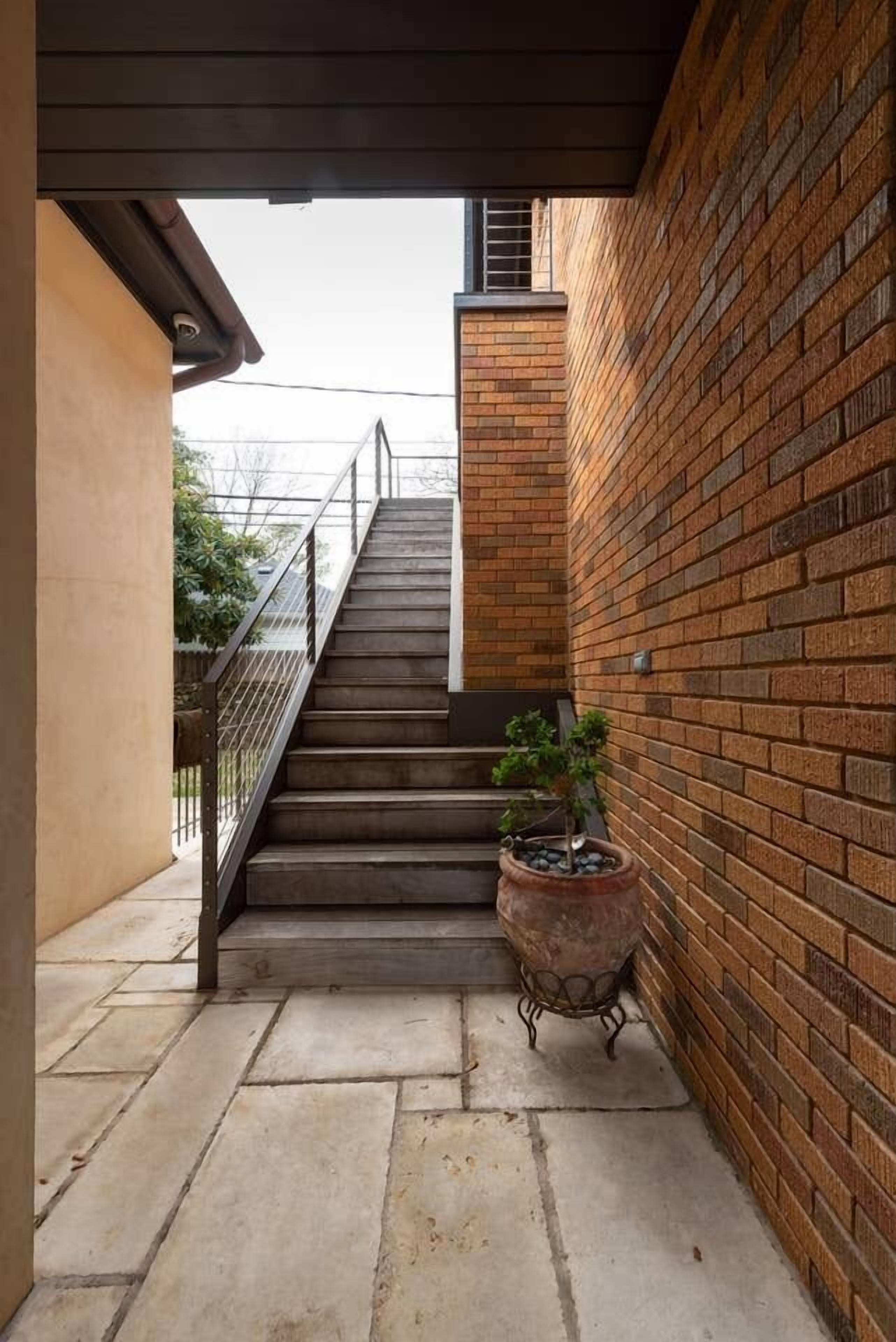 Un escalier menant à un deuxième étage, entouré de murs en briques et agrémenté d’une plante en pot.