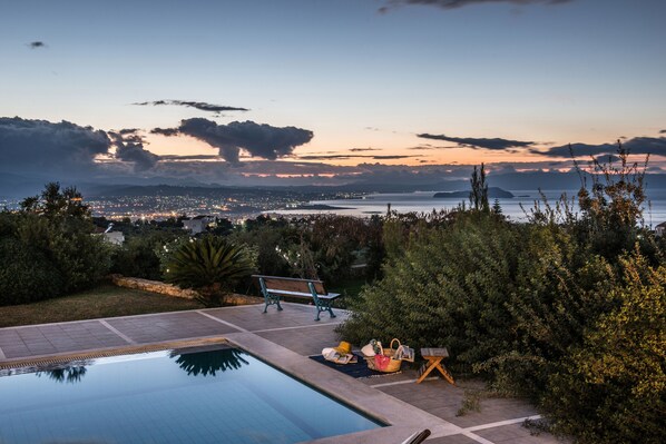 A pool with a bench and lounge chairs, surrounded by greenery and a view of a cityscape at dusk. - Villa Mariposa- Panoramic Sea View - Near Chania City - Private Pool - Spacious  (chania)