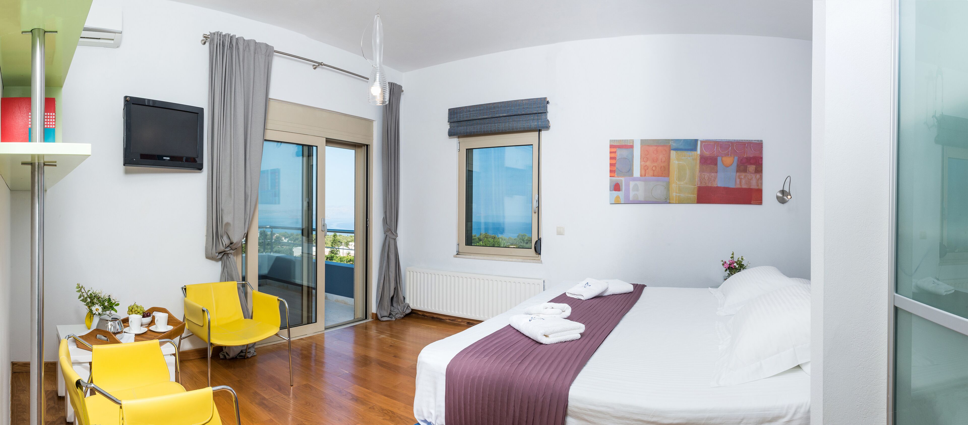 Ein Hotelzimmer mit Bett, einem Sessel, einem Tisch mit einer Vase, einem Fenster und einem Bild an der Wand.