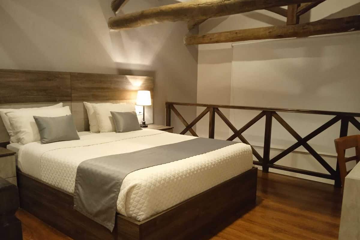 Un dormitorio con estructura de cama de madera, cabecera, mesita de noche con lámpara y baranda de madera.