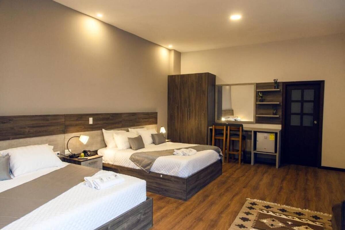 Una habitación de hotel con dos camas, un escritorio, un armario y un espejo.