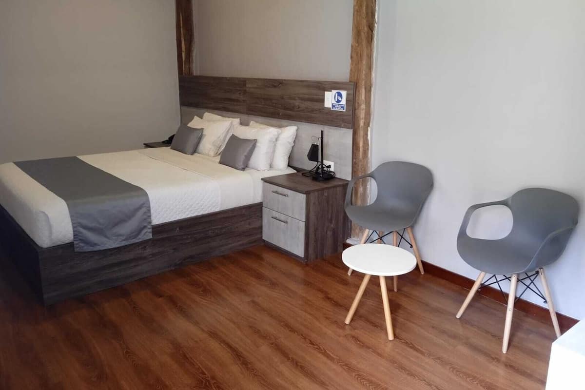 Un dormitorio con cama, mesita de noche, dos sillas y suelo de madera.