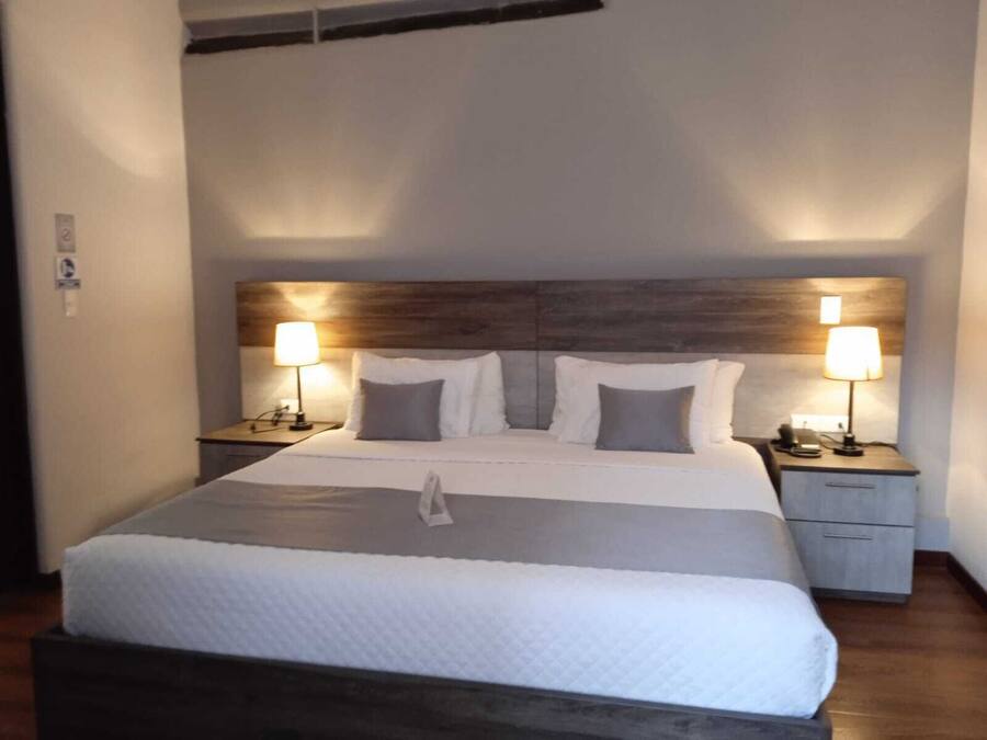 A neatly made bed with a wooden headboard, two bedside tables with lamps, and a small drawer unit.