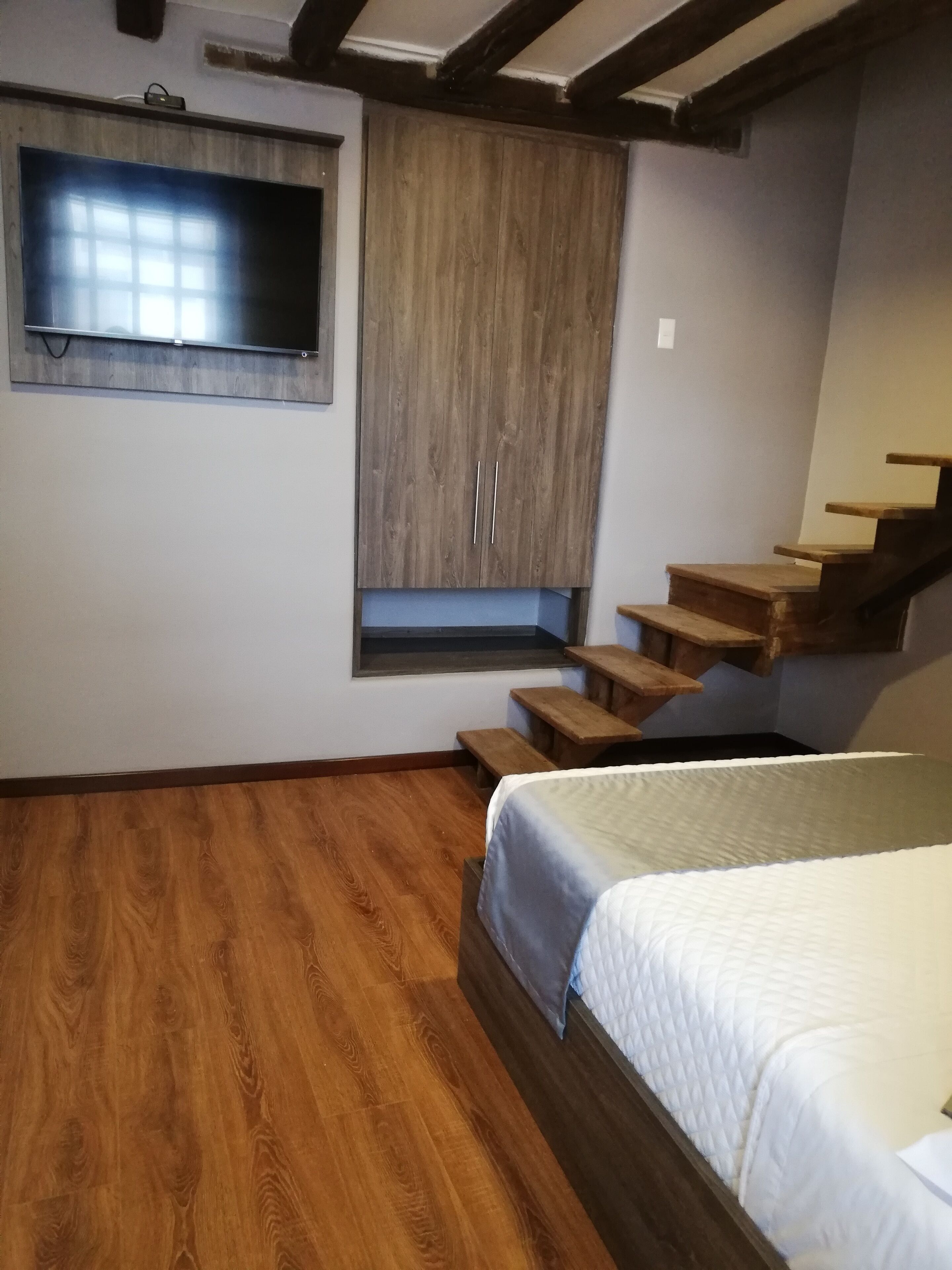 Un dormitorio con piso de madera, una cama con cubierta acolchada, un televisor empotrado y un armario de madera.