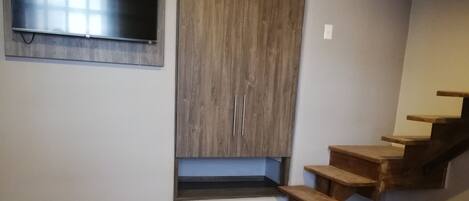 Un dormitorio con piso de madera, una cama con cubierta acolchada, un televisor empotrado y un armario de madera.