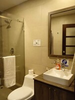 Casa de banho com sanita, lavatório e chuveiro. Há um porta-toalhas com toalha, um dispensador de papel e um dispensador de sabão no lavatório.