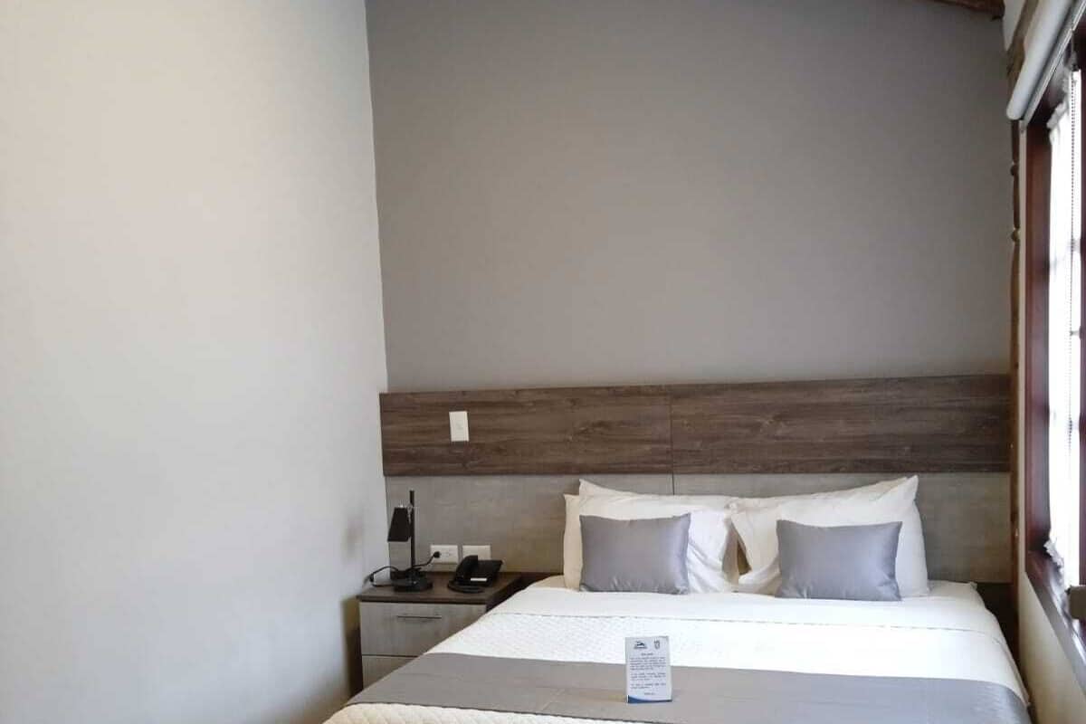 Una habitación de hotel moderna con una cama grande, cabecero de madera y una mesita de noche con lámpara.