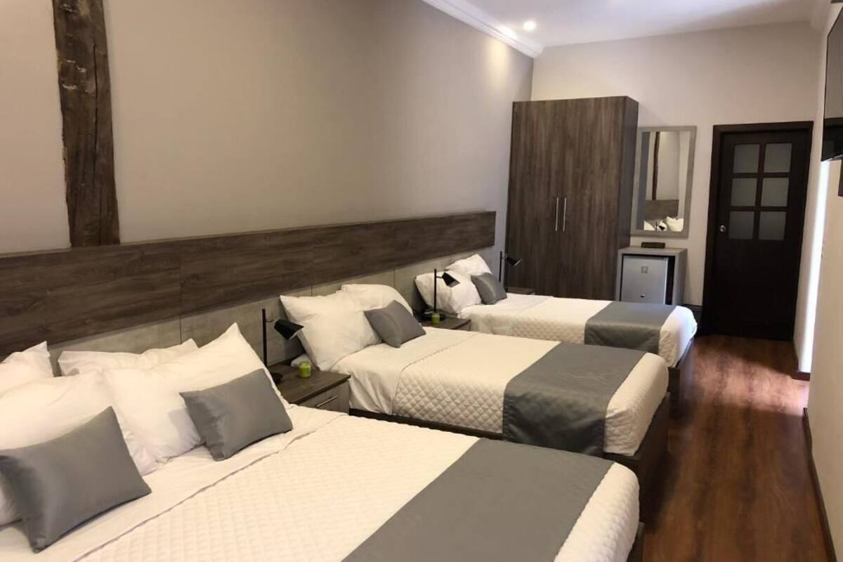 Una habitación de hotel con tres camas, un cabecero de madera, un armario, un espejo y una puerta.
