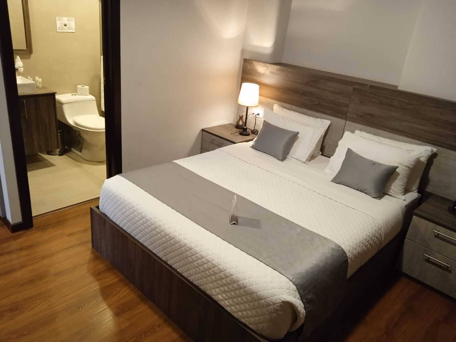 Una camera da letto ordinata con un letto grande, una testata in legno, comodini e un tavolino con una lampada.