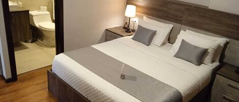 Una camera da letto ordinata con un letto grande, una testata in legno, comodini e un tavolino con una lampada.