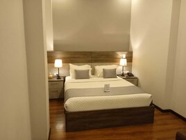 A hotel room with a bed, two bedside tables, a nightstand, and a wooden headboard.