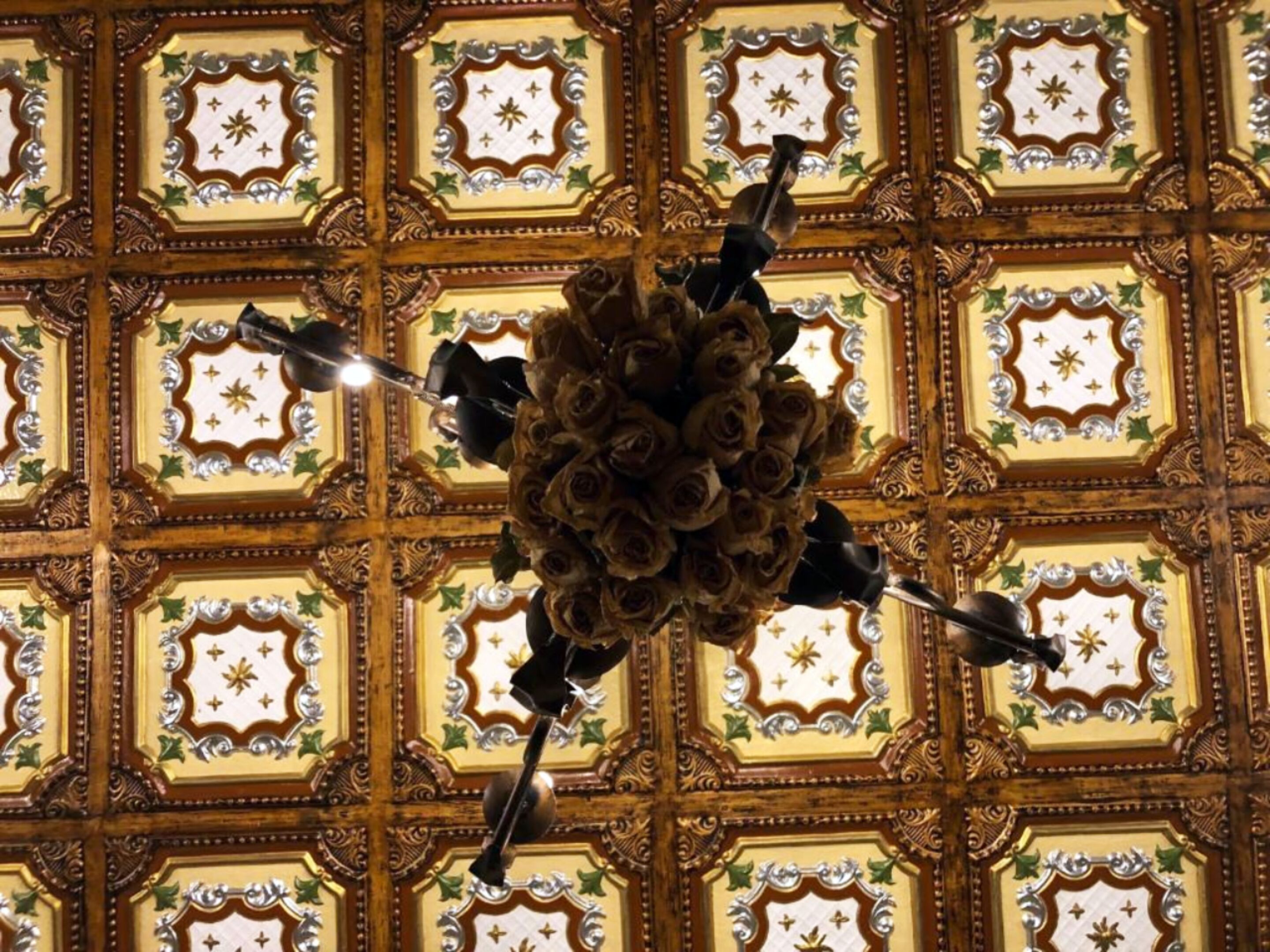 Een plafond met decoratieve geometrische patronen en een bloemarrangement in het midden.