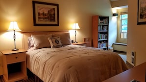 Ein ordentlich eingerichtetes Schlafzimmer mit einem großen Bett, zwei Nachttischen mit Lampen, einem Bücherregal und einem Fenster, das für natürliches Licht sorgt.