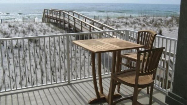 A wooden deck with a table and chairs overlooking a beach with dunes. - Beach Front/First Row on the Gulf of Mexico, next to the Dune Crossover. 2B/2B (Pensacola Beach)