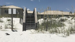 A sandy beach with a wooden staircase leading to a building with a sloped roof. - Beach Front/First Row on the Gulf of Mexico, next to the Dune Crossover. 2B/2B (Pensacola Beach)