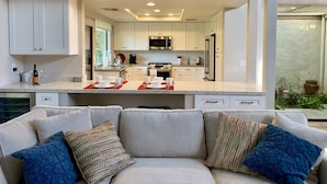 A modern kitchen with white cabinets, stainless steel appliances, and a central island with a coffee maker and cups. - Beautifully Renovated 2/2 in Monterey CC with Mountain Views (Palm Desert)