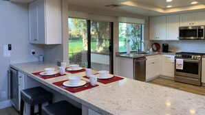 A modern kitchen with a large island, stainless steel appliances, and a view of a green landscape. - Beautifully Renovated 2/2 in Monterey CC with Mountain Views (Palm Desert)