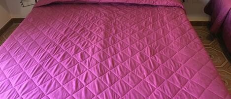 A bed with a pink quilted bedspread and matching pillows.