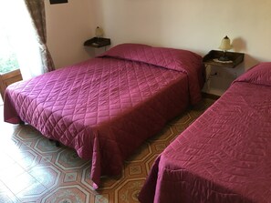 Two beds with matching purple bedding, a nightstand with a lamp, and patterned floor tiles. - Al Chiaro di Luna (Taormina)