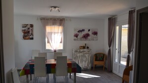 A dining area with a table set for four, a cabinet, and a chair with a cushion. - Gîte with barbecue and enclosed terrace close to shops and rivers (Lagorce)
