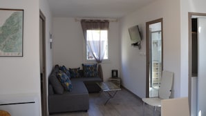 A living room with a sofa, a coffee table, a TV mounted on the wall, and a window with curtains. - Gîte with barbecue and enclosed terrace close to shops and rivers (Lagorce)
