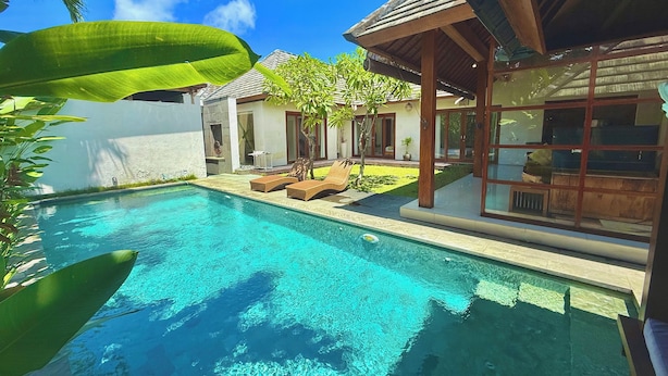 A swimming pool with clear water, surrounded by a wooden deck and lounge chairs.