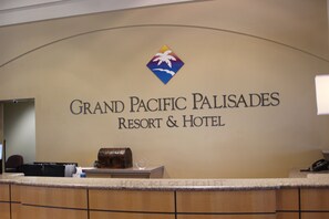 A reception desk at Grand Pacific Palisades Resort & Hotel with a logo above the name, a wooden counter, and a telephone on the right.