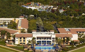 A resort with a swimming pool, multiple buildings, and a theme park in the background.
