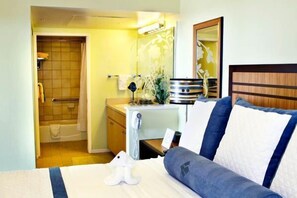 Ein Hotelzimmer mit Bett, Nachttisch, Spiegel, Duschbereich und kleinem Schreibtisch mit Telefon.