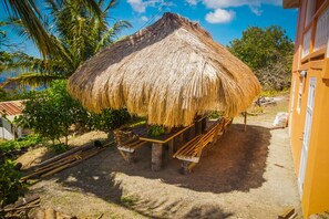 Una estructura con techo de paja, con bancos, rodeada de palmeras y un cielo despejado.