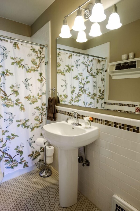 A bathroom with a white sink, a mirror, and a shower curtain with a floral pattern. - Bluebird Day - Riverside Cottage, Relax at a cozy 3-bedroom retreat in Bend, OR. (Bend)