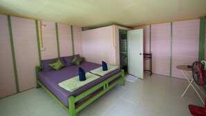 Een kamer met een bed, een tafeltje, een ventilator en een deur naar een badkamer.