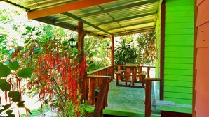 Een overdekt buitengebied met een houten bank en tafel, omringd door weelderige beplanting en een groene wand.