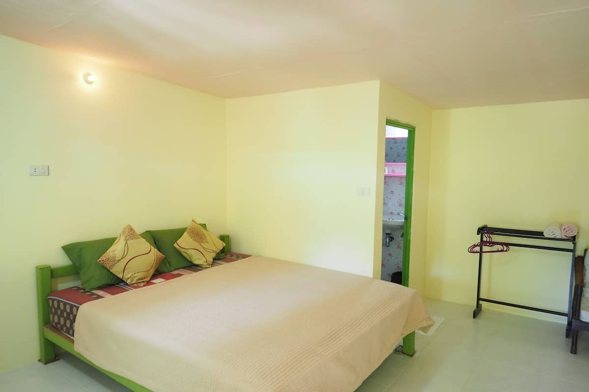 A room with a bed, a small table with a towel rack, and a door leading to a bathroom.