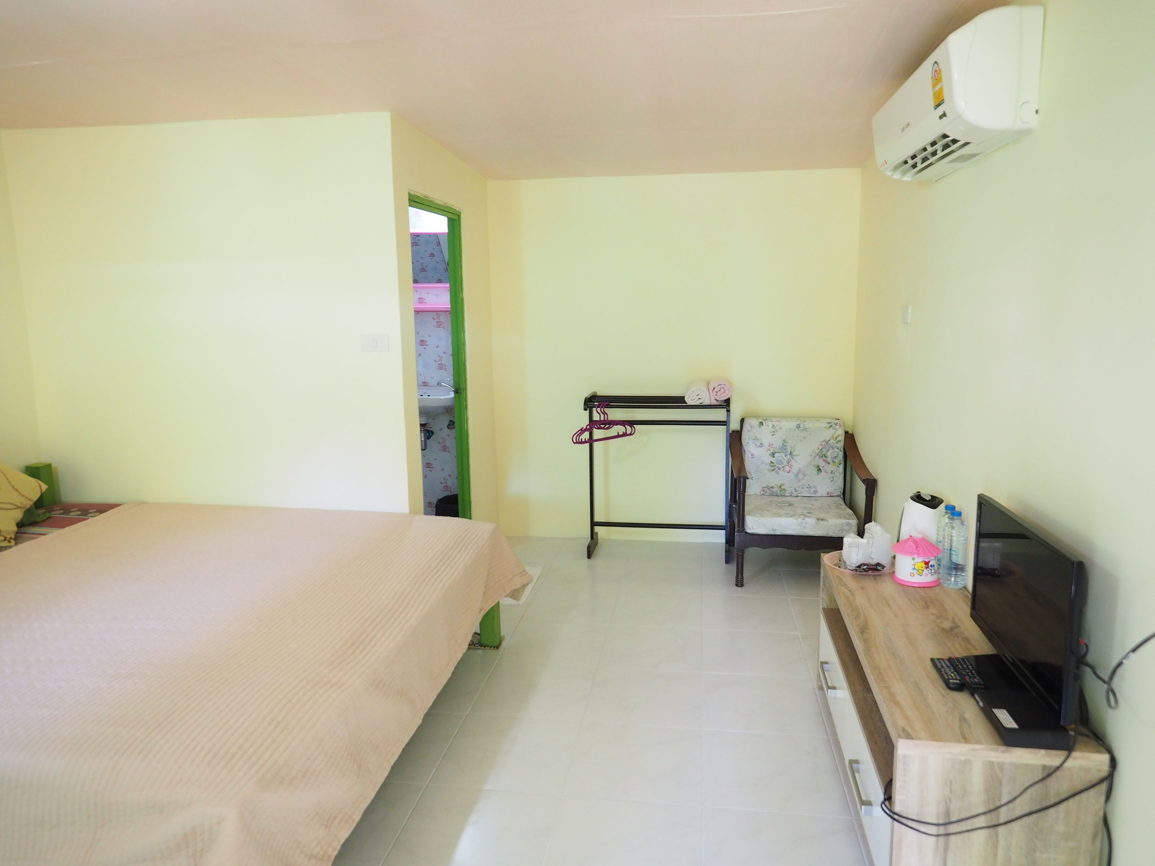Una habitación con cama, una silla, un escritorio con computadora y aire acondicionado.