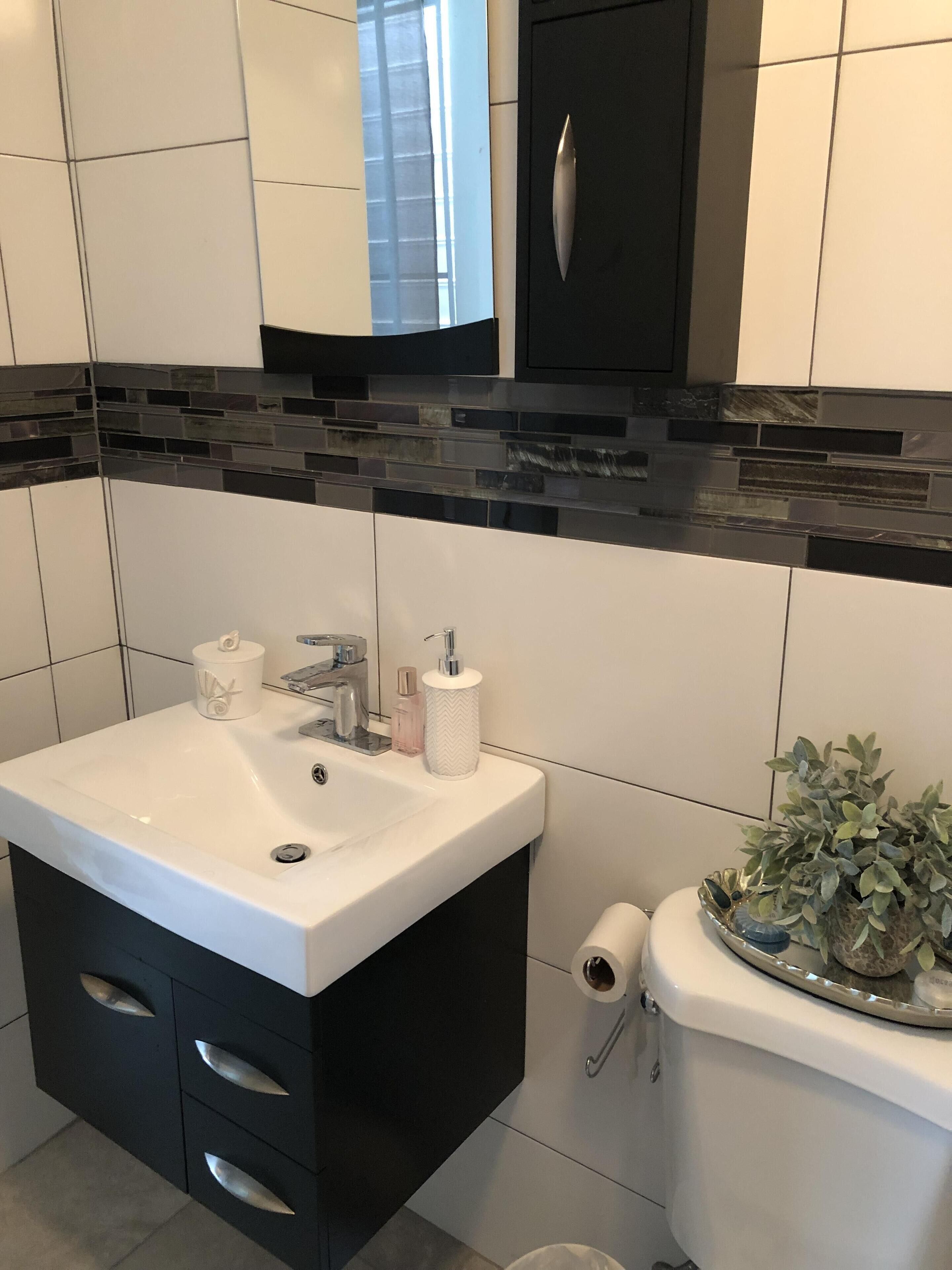 A modern bathroom with a white sink, black cabinet, and a decorative backsplash.
