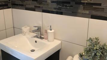 A modern bathroom with a white sink, black cabinet, and a decorative backsplash.