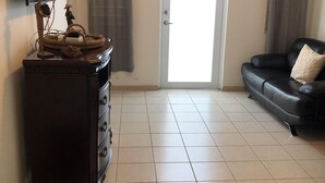 Un salón con un mueble de madera oscura, un sofá de cuero negro, un televisor montado en la pared y un ventilador de techo.