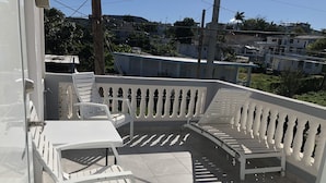 Un balcón con mobiliario de plástico blanco, que incluye una mesa y sillas, y barandilla blanca.