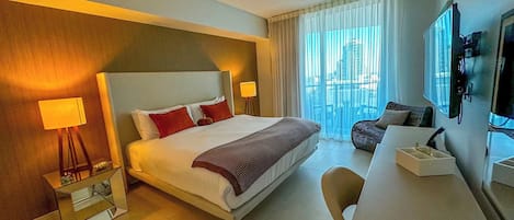 Habitación de hotel con una cama grande, dos lámparas de noche, un televisor de pantalla plana, un sofá y vistas a la ciudad por la ventana.