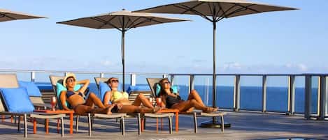 Un espace aménagé au bord de la piscine, avec des chaises longues et des parasols, donnant sur une étendue d’eau.