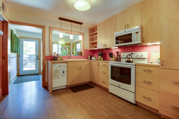 A kitchen with wooden cabinets, a microwave, a kettle, and a dishwasher.